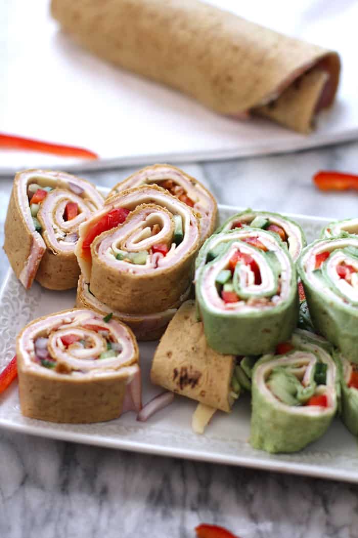 Side shot of a tray of turkey club roll ups, with an uncut one in the background.