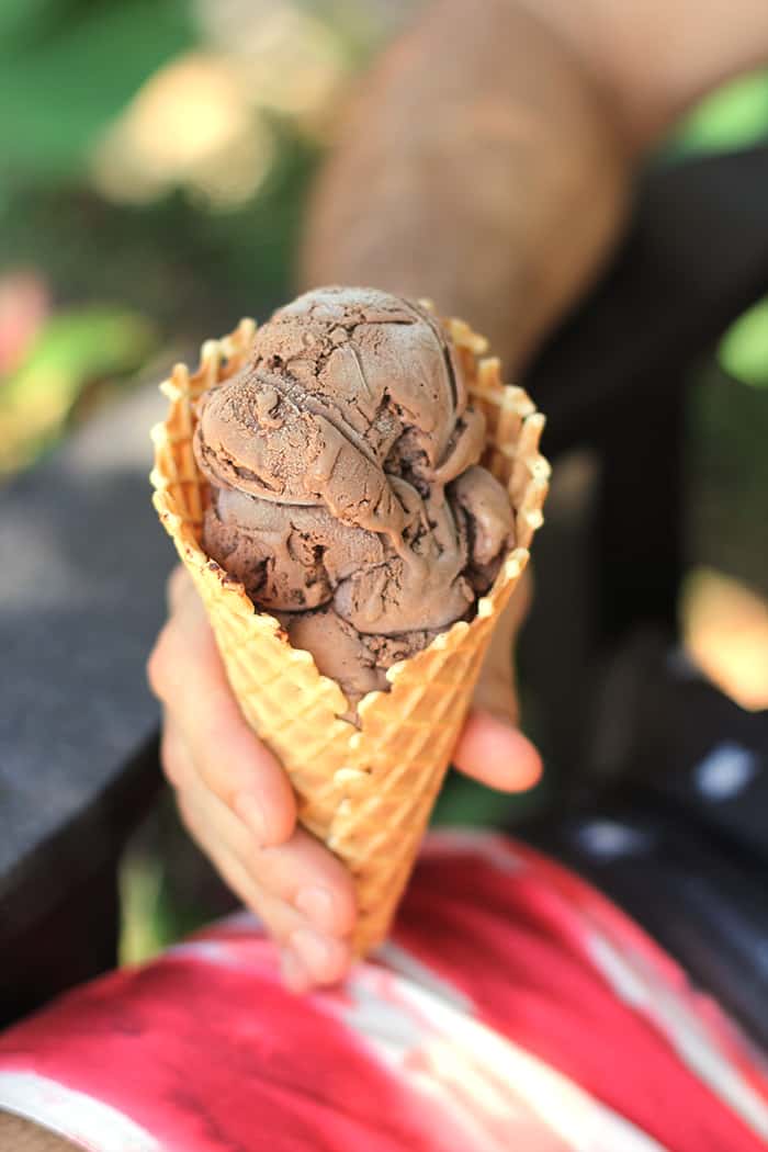 Side shot of a man sitting outside, holding a waffle cone filled with homemade double chocolate ice cream.