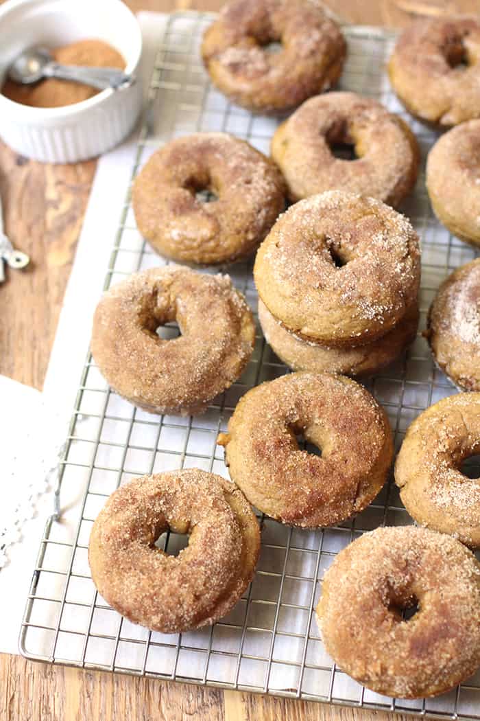 Overhead shot of pumpkin donuts on a baking rack, over white napkin on wooden board.