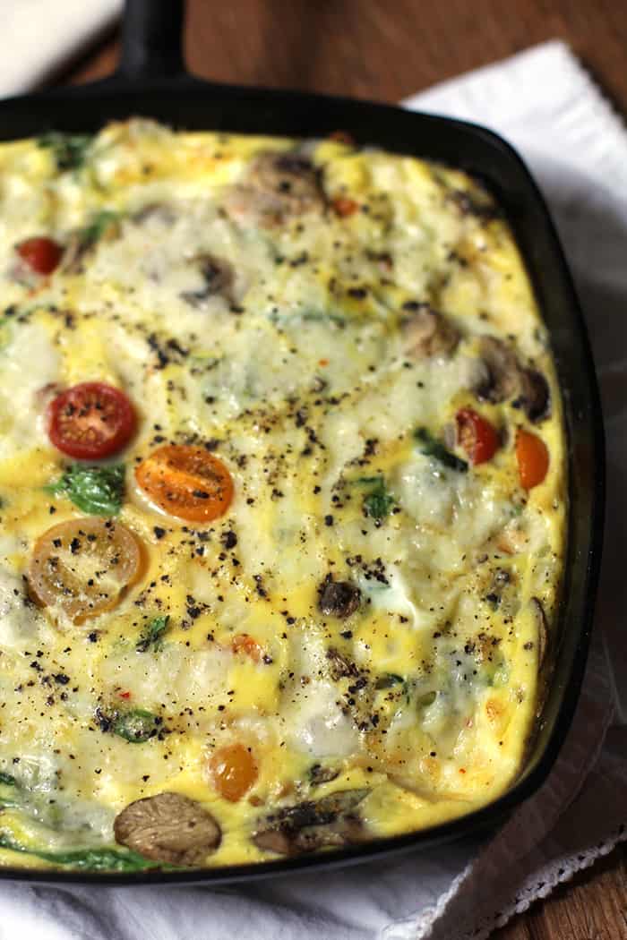 Closeup shot of a cast iron skillet of creamy vegetable frittata, on a white napkin.