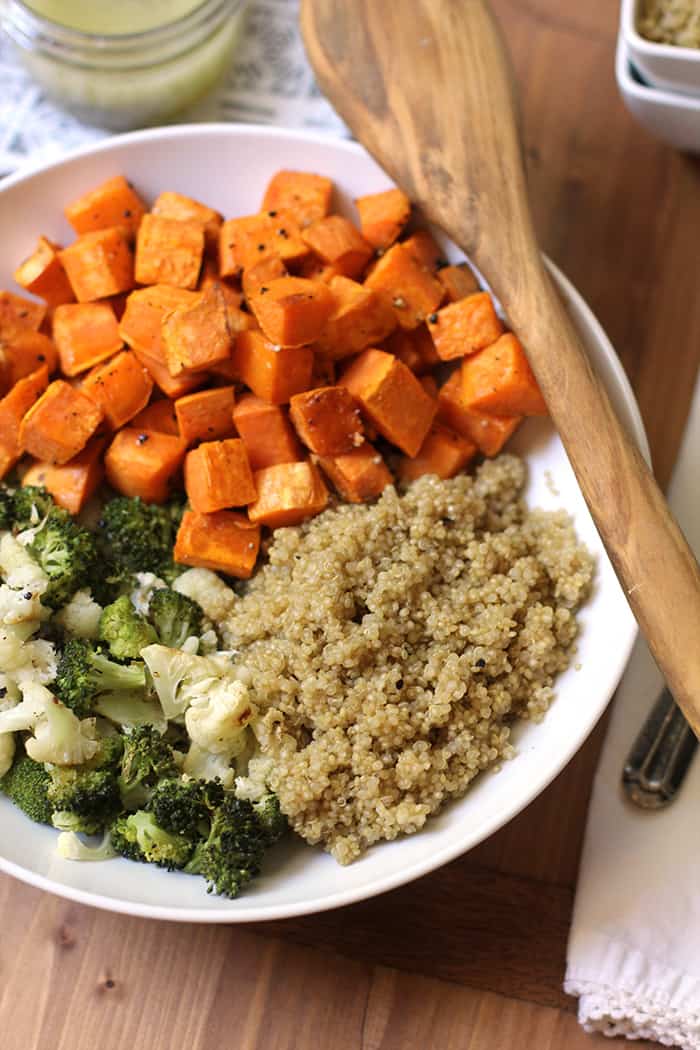 Overhead shot of a white bowl of roasted sweet potatoes, broccoli, cauliflower, and cooked quinoa.