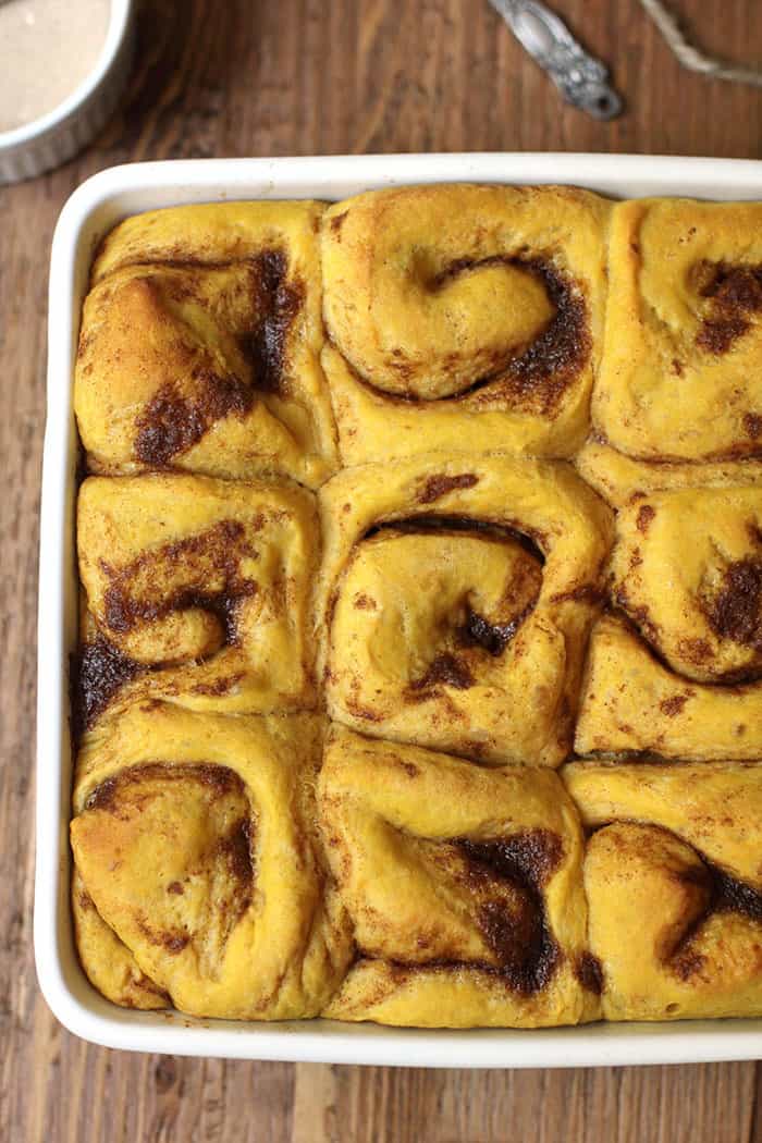 Close-up shot of pumpkin cinnamon rolls in a square white dish, on a wooden background.