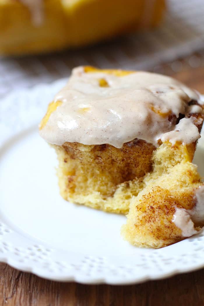 Close-up side view of one pumpkin cinnamon roll with frosting, on a white plate