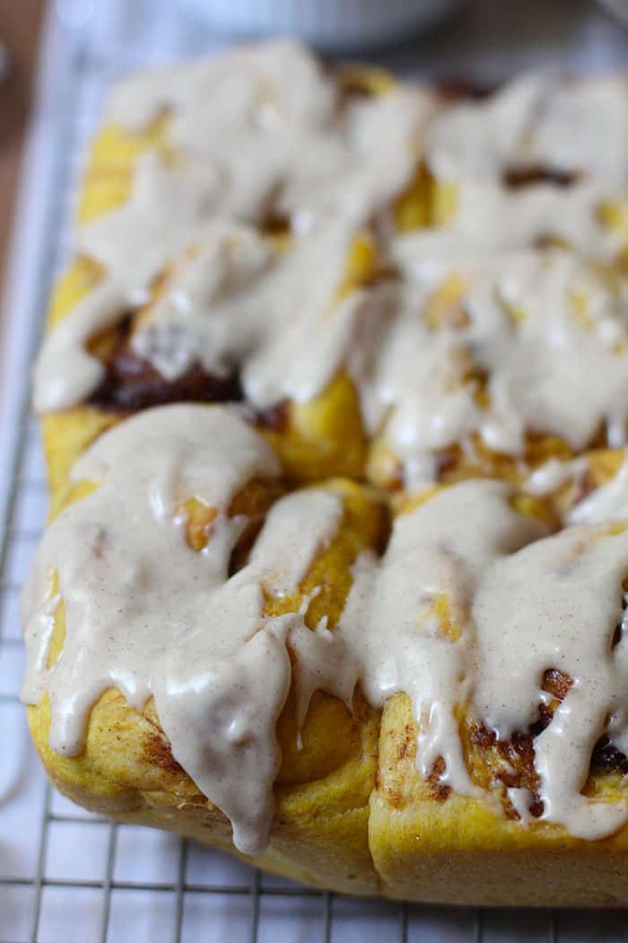 Side angle of pumpkin cinnamon rolls with icing, on a wire rack.