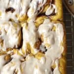 Close-up shot of pumpkin cinnamon rolls with icing on top, all on a wire rack.