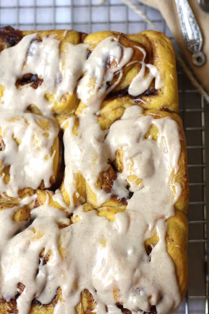 Close-up shot of pumpkin cinnamon rolls with icing on top, all on a wire rack.