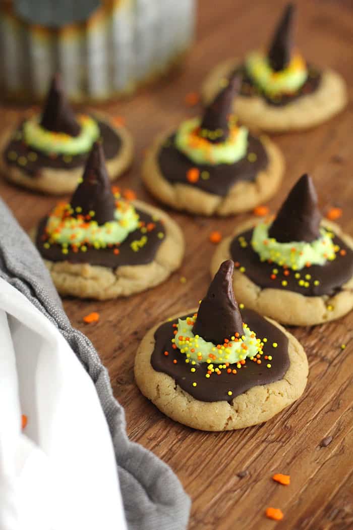 Side angle of witch hat peanut butter cookies on a wooden background, with a halloween decoration in the background.