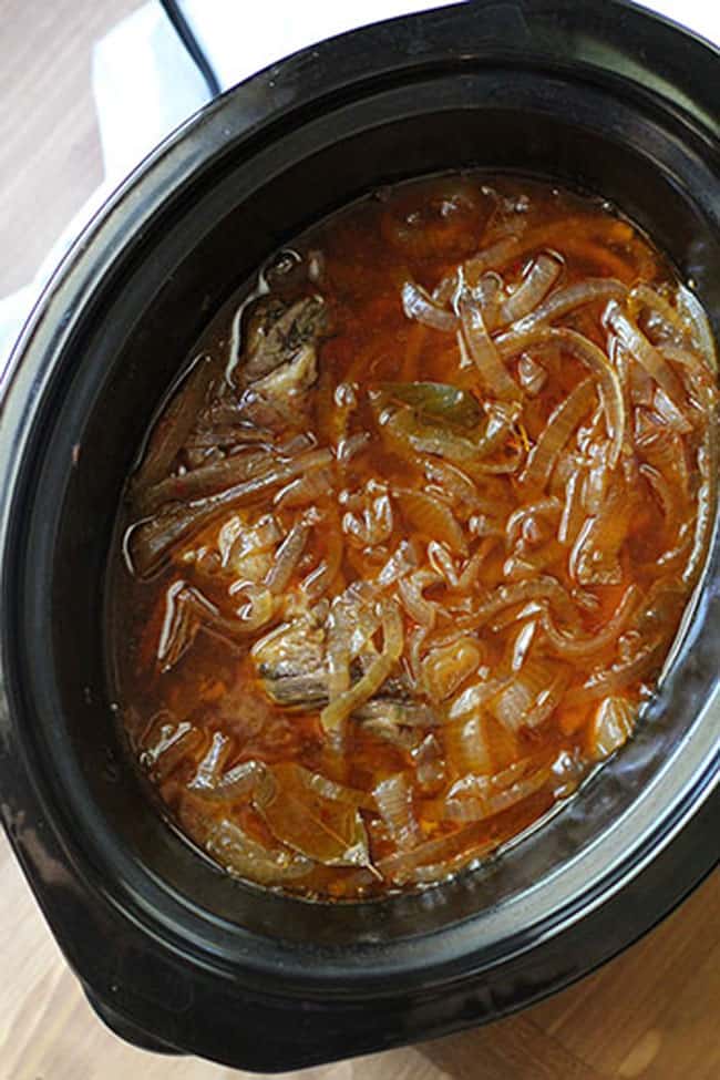 Overhead shot of a black crock pot full of beef au jus, on a wooden background.