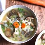 Overhead shot of a bowl of detox chicken vegetable soup, on a wooden background with whole carrots beside the bowl.