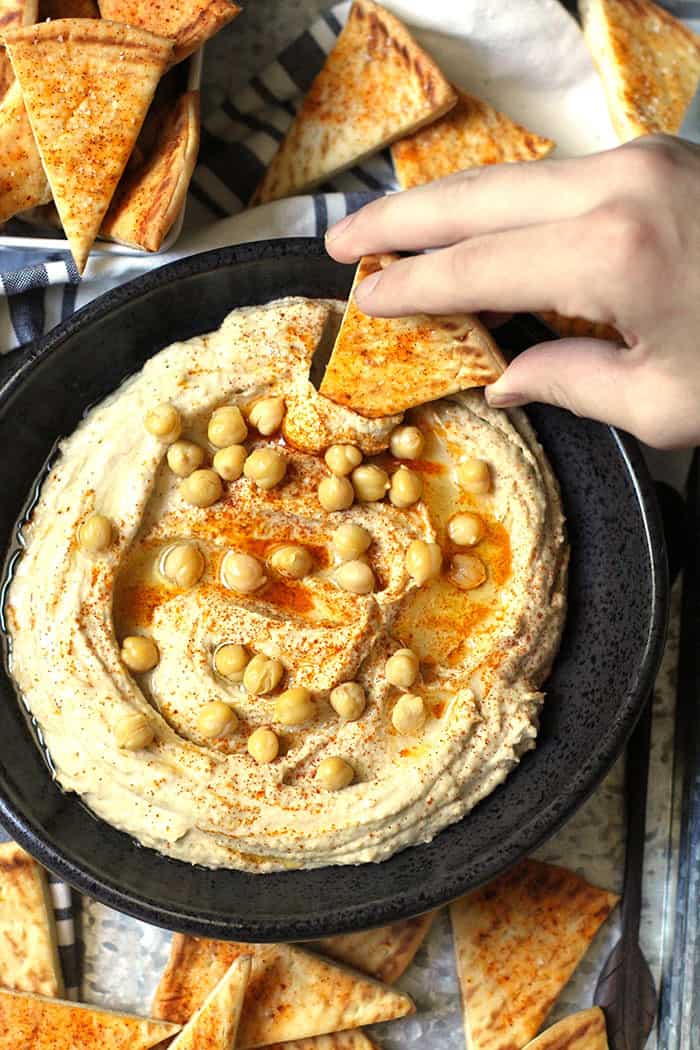 A hand dipping a pita bread into some homemade hummus.