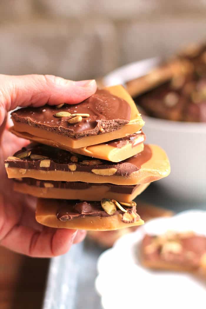 Close-up shot of my hand holding a stack of five pieces of toffee, with a brick wall in the background.