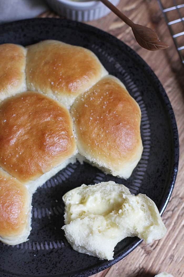 Overhead shot of homemade dinner rolls on a black plate, with one roll buttered.