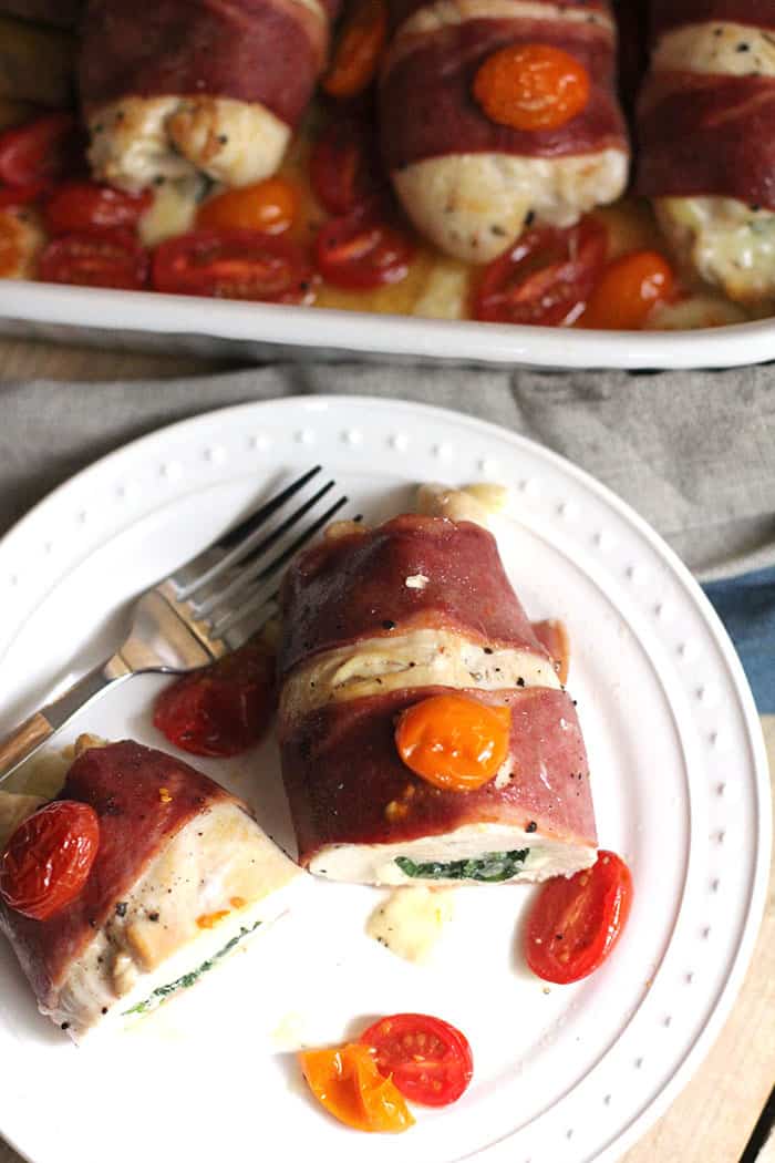 Overhead shot of a white plate with one bacon wrapped chicken breast cut in half, with a portion of the casserole in the background.