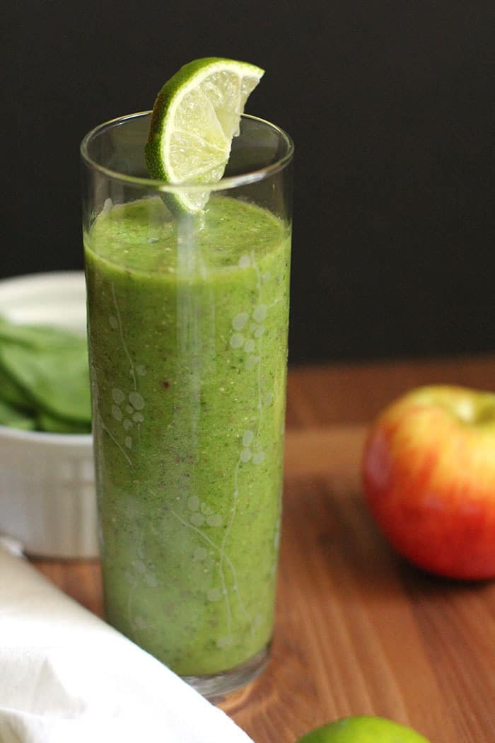One tall glass of green smoothie, on a wooden board.