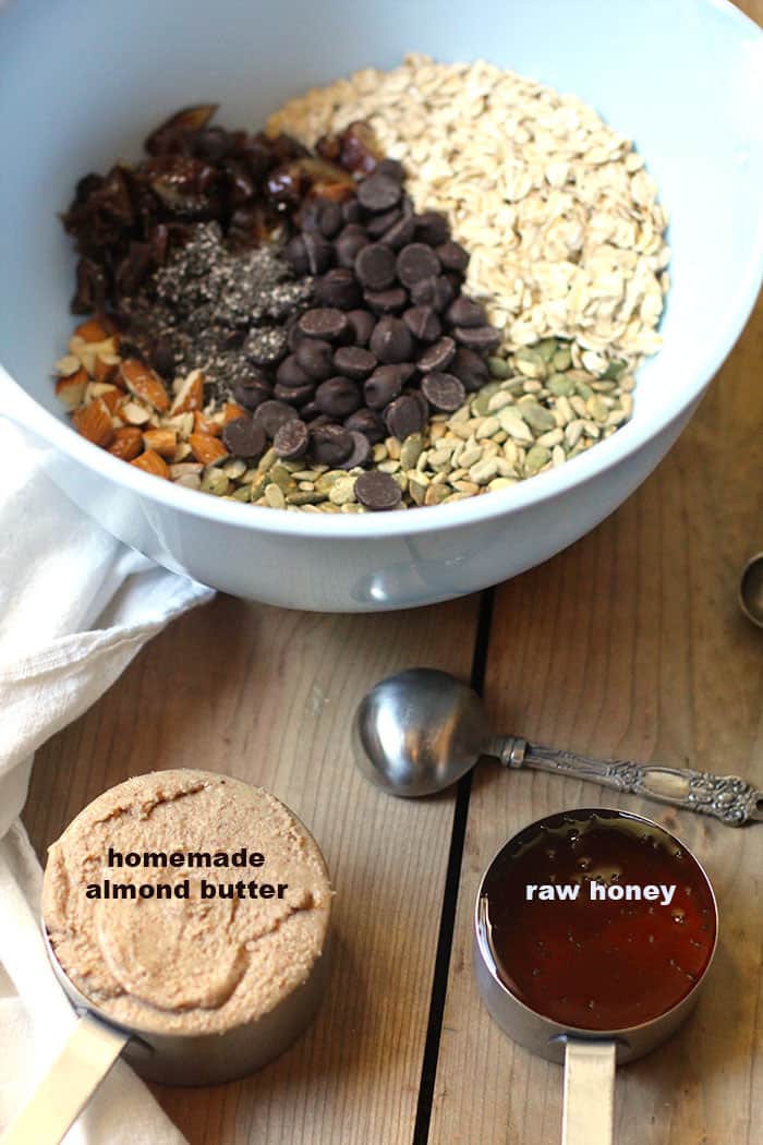 A blue mixing bowl full of energy bite ingredients, with a measuring cup of homemade almond butter and one of raw honey.