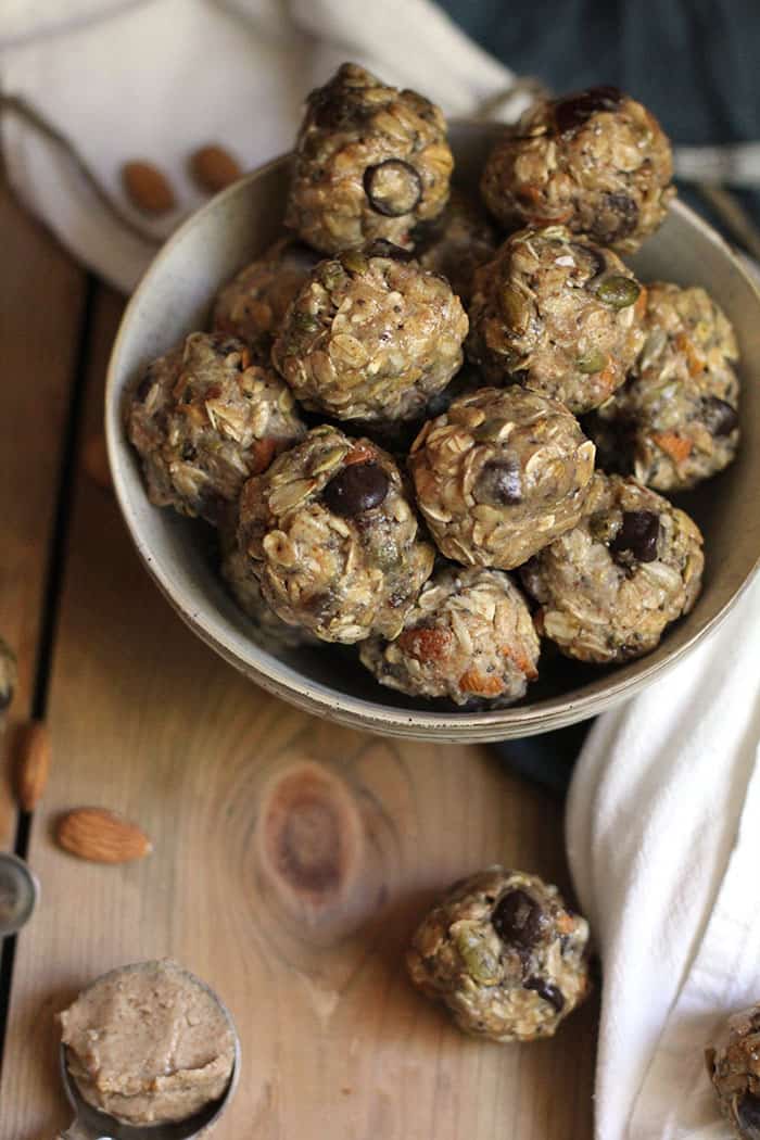 Overhead shot of a bowl of almond butter energy bites, on a wooden background with a white towel.