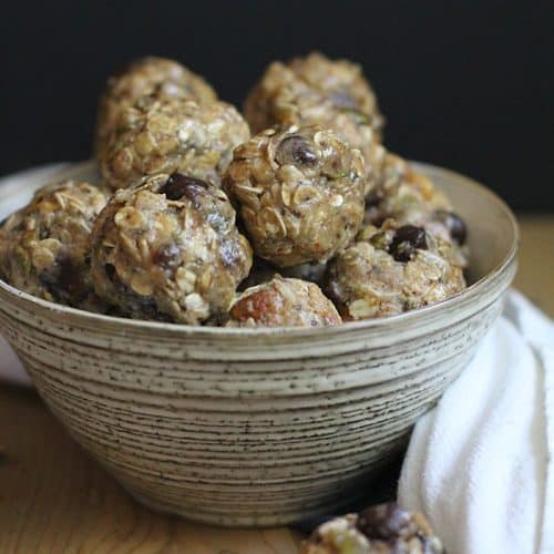 A side shot of a bowl of almond butter energy bites, on a wooden background with a white towel.