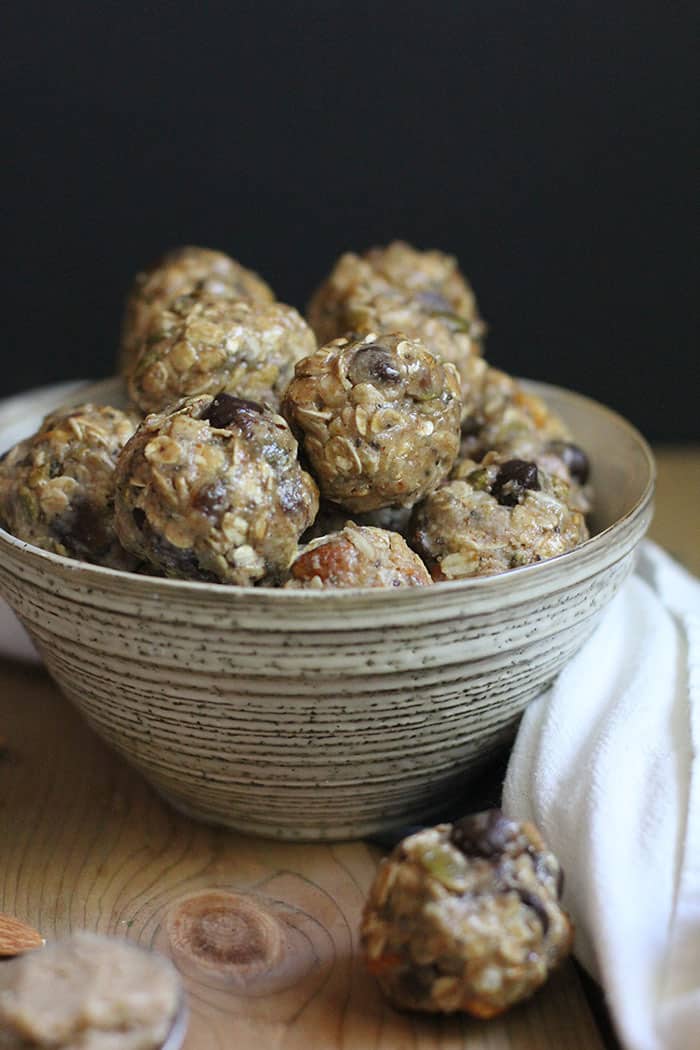 A side shot of a bowl of almond butter energy bites, on a wooden background with a white towel.