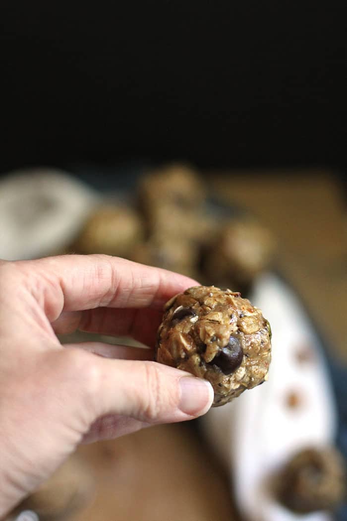 My hand holding an almond butter energy bite, with a wooden board in the background.