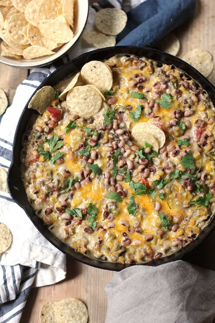 Overhead shot of a cast iron skillet filled with a cheesy black-eyed pea dip, with Tostitos chips next to it, on a wooden background.