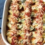 Side shot of a casserole dish of turkey sausage and spinach stuffed shells, with pasta sauce on top.