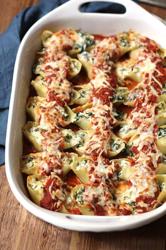 Side shot of a casserole dish of turkey sausage and spinach stuffed shells, with pasta sauce on top.