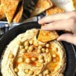 A hand dipping a pita bread into a bowl of homemade hummus.