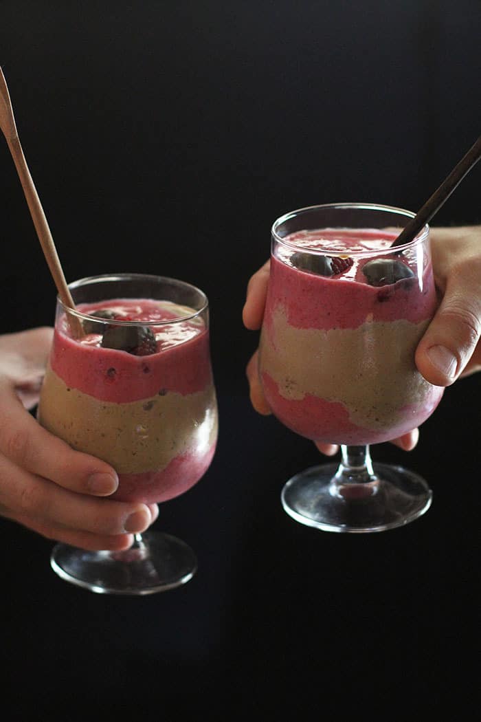 Side view of two hands holding Nutella Raspberry Smoothies, with a black background.