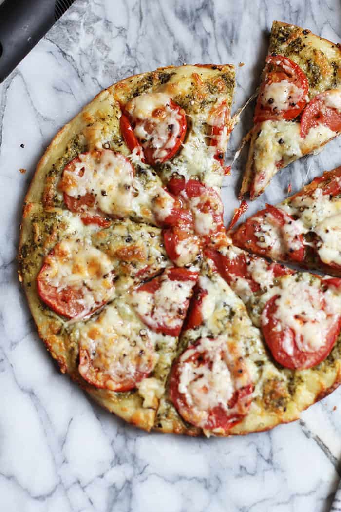 Overhead shot of a pesto tomato pizza on a marble board, cut into 8 slices.