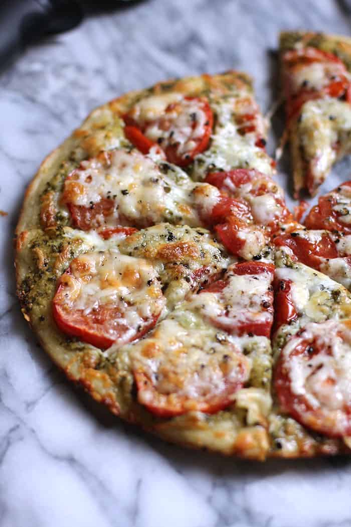 Side shot of a sliced pesto tomato pizza.