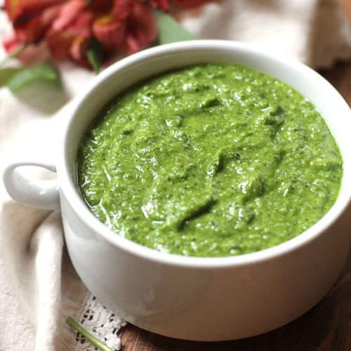 A bowl of spinach walnut pesto sauce in a white bowl, on a brown board.