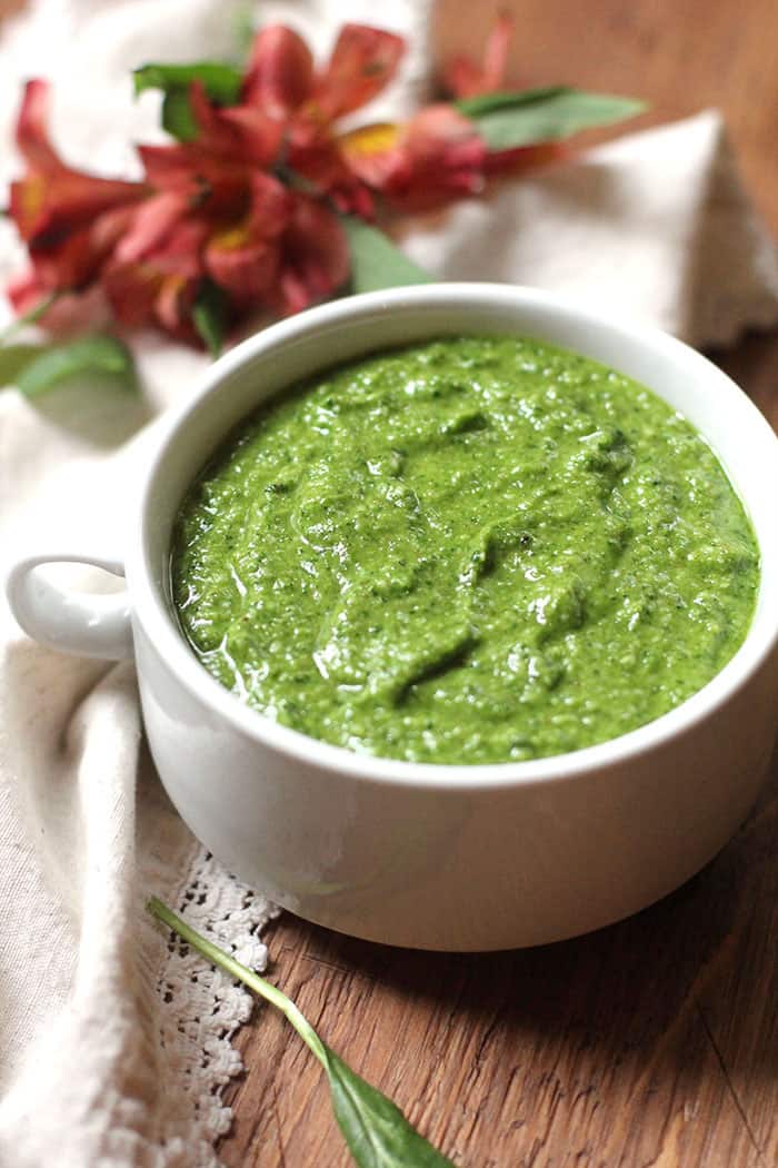 A bowl of spinach walnut pesto sauce in a white bowl, on a brown board.