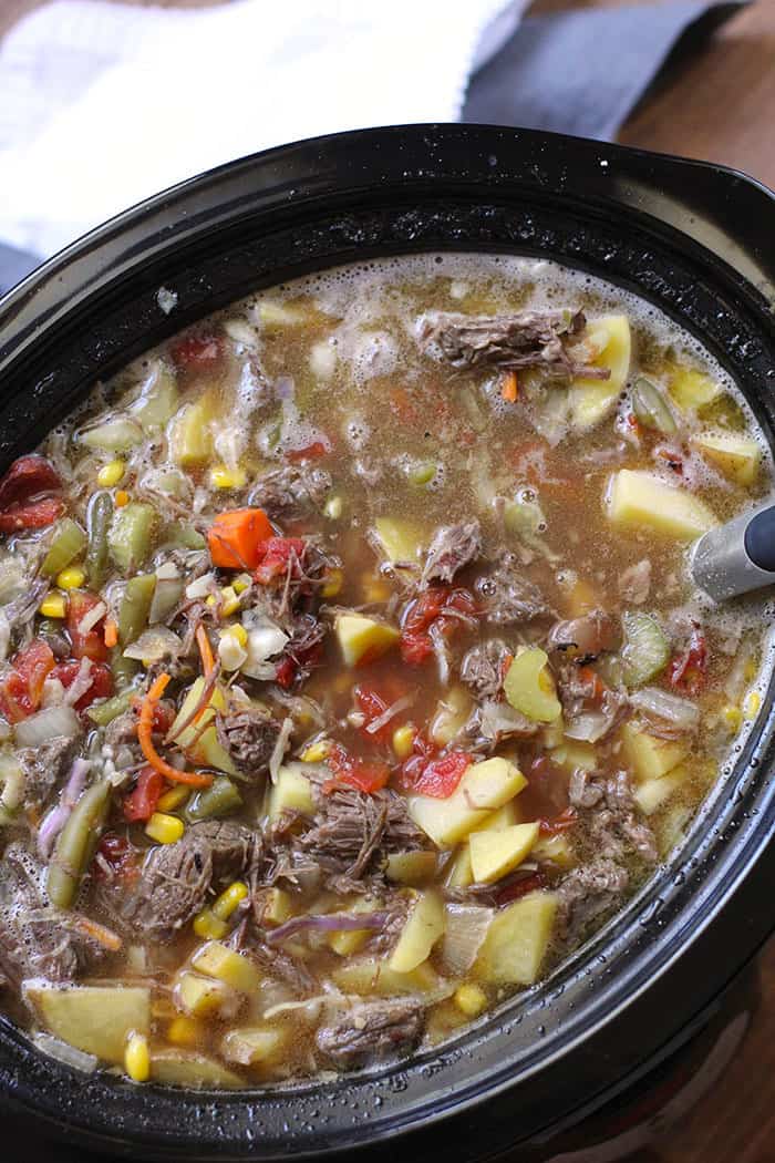 Overhead shot of a slow cooker filled vegetable beef soup, with a large spoon inside.