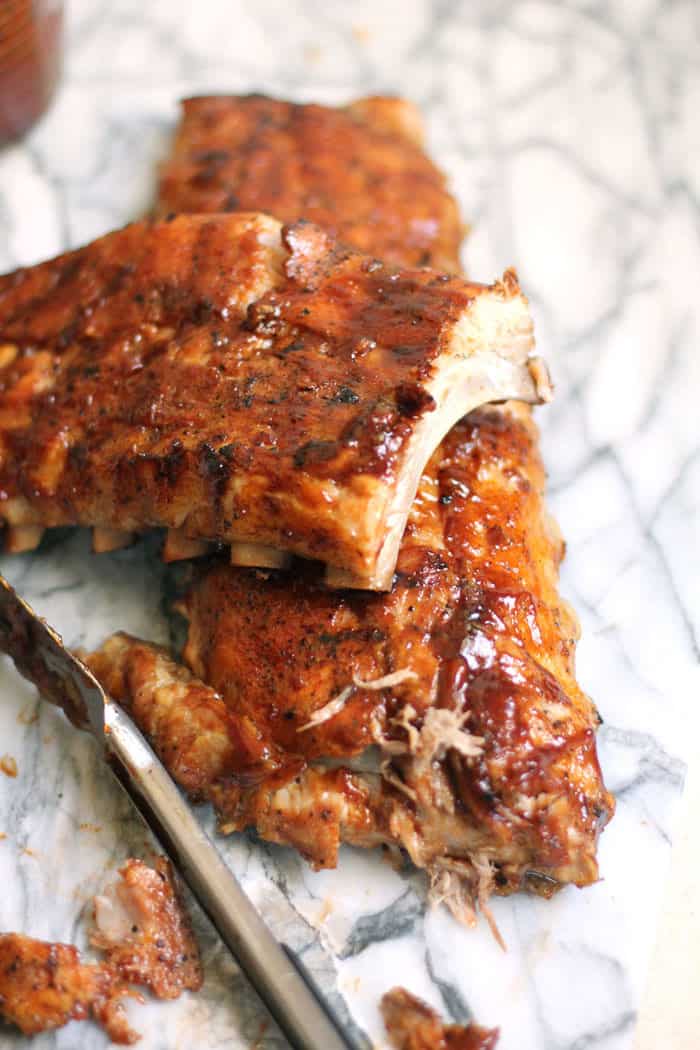 Two racks of barbecue baby back ribs, on a white board.