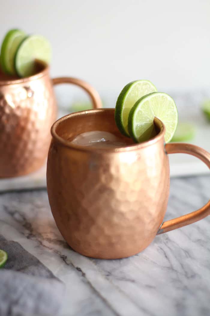 Side shot of two copper mugs with classic Moscow mules, and lime slices.