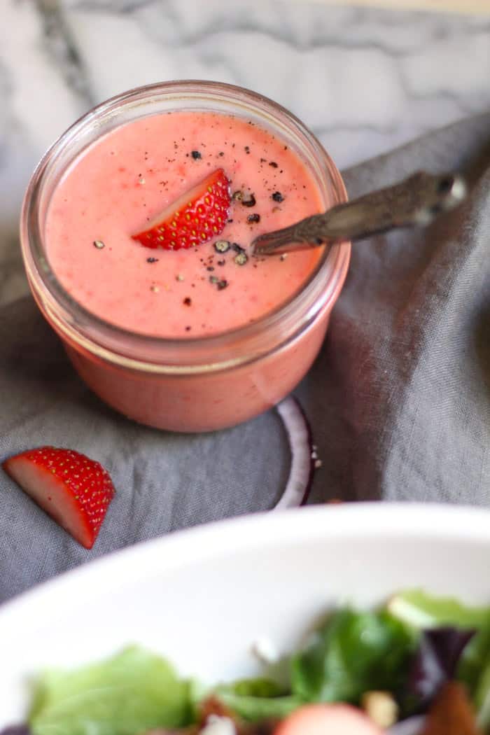 A small mason jar of creamy strawberry dressing with a spoon inside.