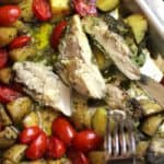 Close-up overhead shot of a sheet pan of pesto chicken, potatoes and tomatoes, with the chicken cut into pieces.