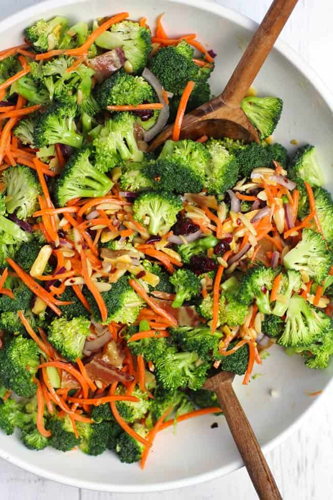 Overhead shot of a large white salad bowl filled with broccoli salad, with salad tons inside.