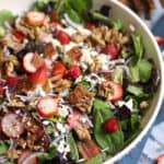 Overhead shot of a large white bowl of strawberry bacon salad with a jar of creamy strawberry dressing beside it.