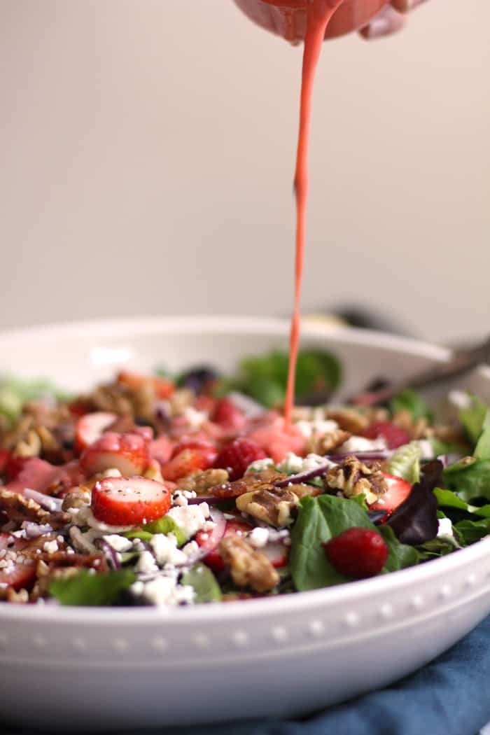 Side shot of a drizzle of creamy strawberry dressing over a large strawberry bacon salad.