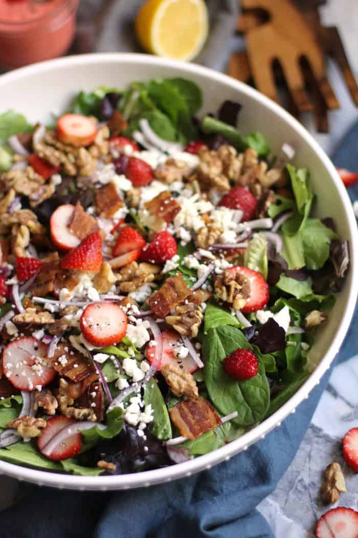 Overhead shot of a large white bowl of strawberry bacon salad with a jar of creamy strawberry dressing beside it.