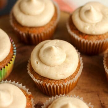 Overhead view of carrot cake cupcakes with cream cheese frosting on a wooden background.