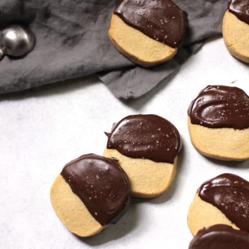 Overhead view of shortbread cookies dipped in chocolate, on a white background with gray napkin.