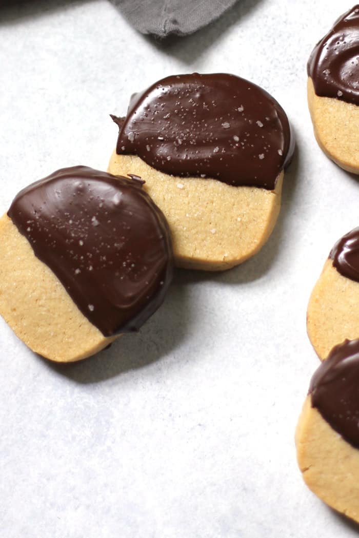 Close-up view of shortbread cookies dipped in chocolate, on a white background with gray napkin.