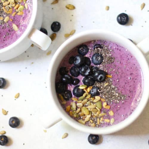 Two blueberry smoothie bowls on a white background.