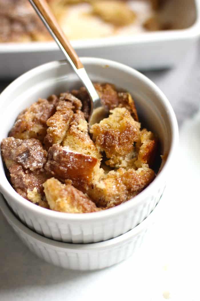 Overhead shot of one serving of French toast casserole in round serving dish stacked on top of another one, with a fork inside, and the casserole in the background.