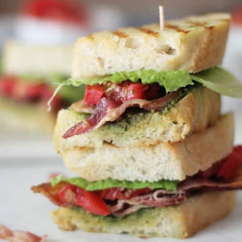 A double stack of BLT pesto sandwich on a white surface.