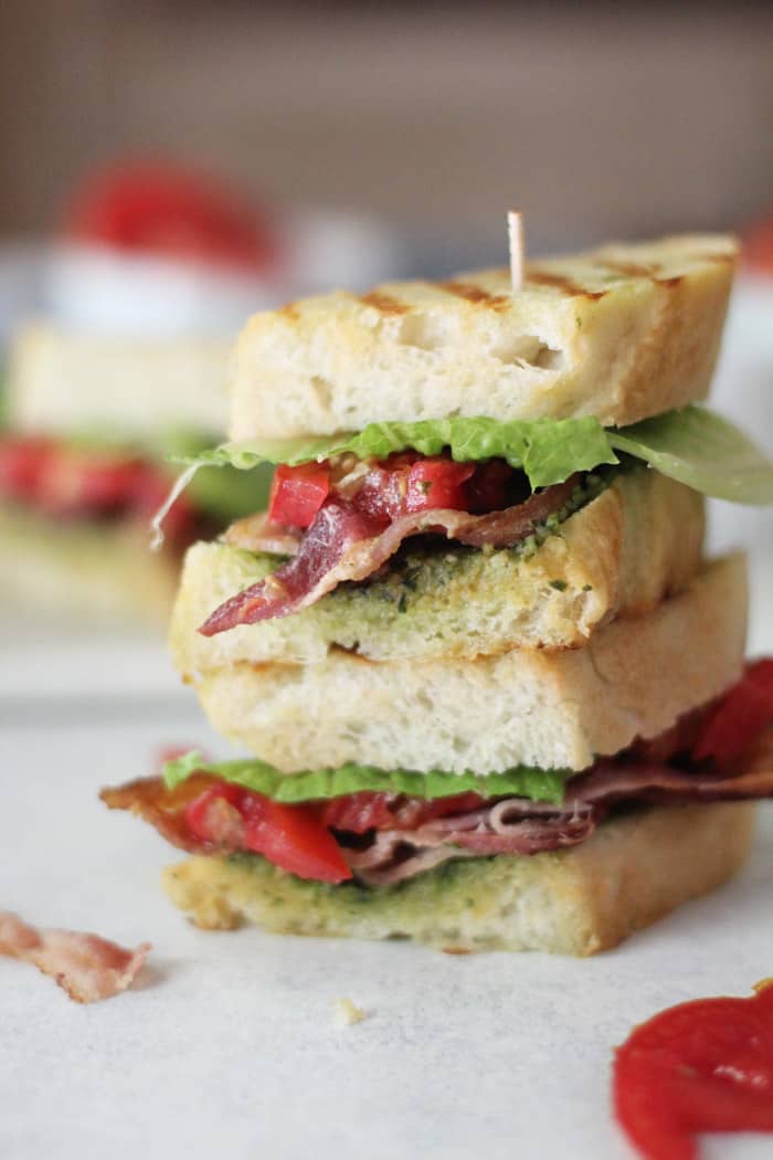 A double stack of BLT pesto sandwich on a white surface.