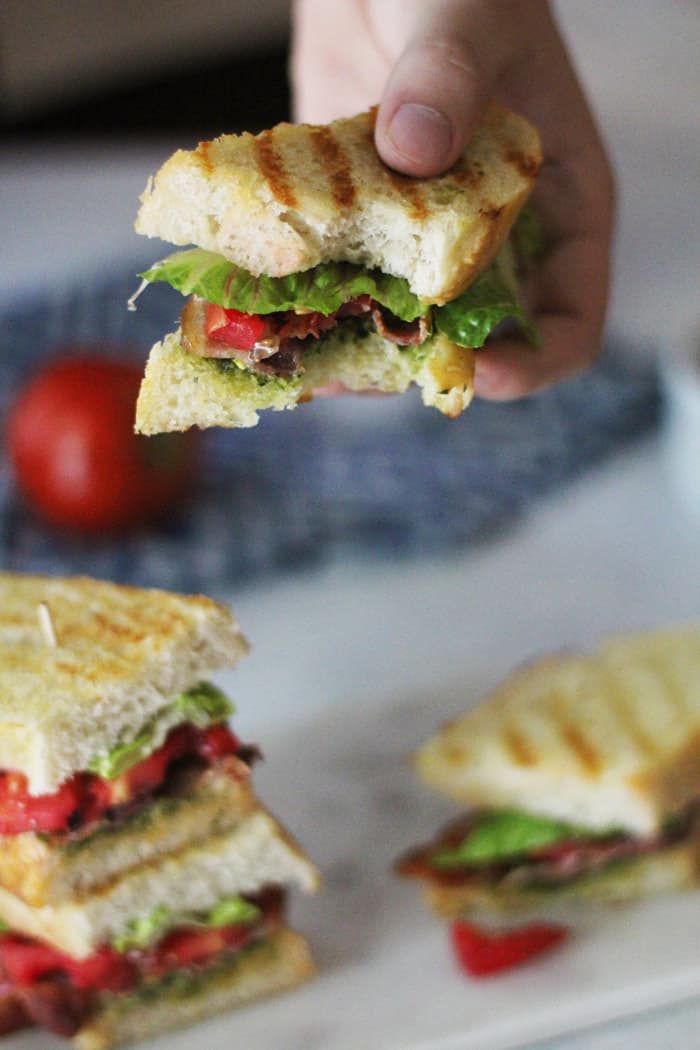 A hand holding a partially eaten BLT pesto sandwich.