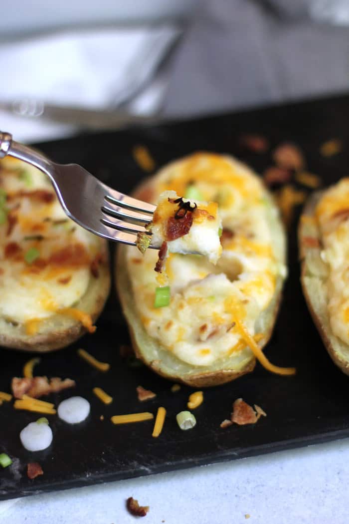 Side angle of three twice baked potatoes on a black tray, with a forkful of one potato
